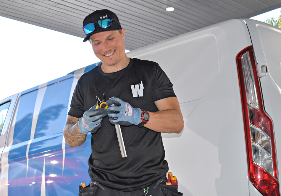 Kuvassa Wirmaxin asennustyöntekijä seisoo pakettiauton edessä ja hymyilee.