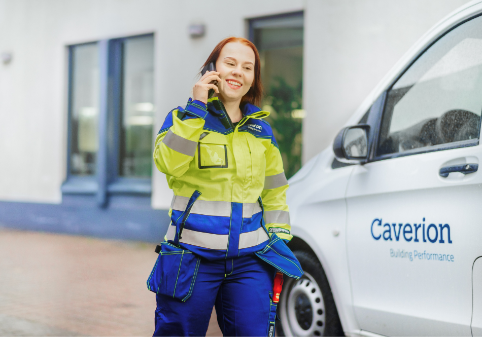 Kylmäasentajana työskentelevä nainen kävelee työvaatteissa kohti valkoista pakettiautoa, jossa lukee Caverion. Kävellessään asentaja puhuu kännykkään ja hymyilee.