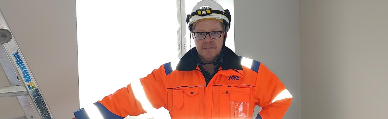 Jouni Riikola seisoo talotekniikkakohteessa työvaatteissa. Hän katsoo kameraan, ja hänellä on päässään suojakypärä. Kuva on artikkelin kansikuva, joten se rajautuu siten, että Jounista näkyy ainoastaan ylävartalo.
