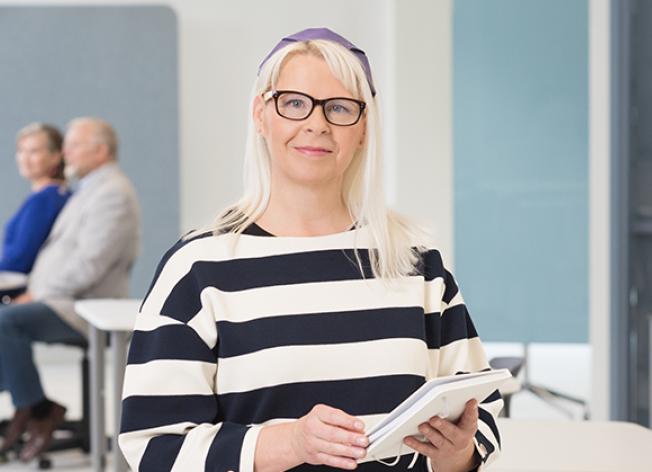 Nainen katsoo kameraan, taustalla ihmisiä