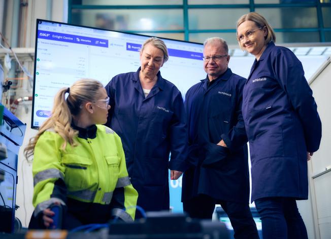 Työtakkinen nainen esittelee teollisuuspumppua kolmelle opiskelijalle