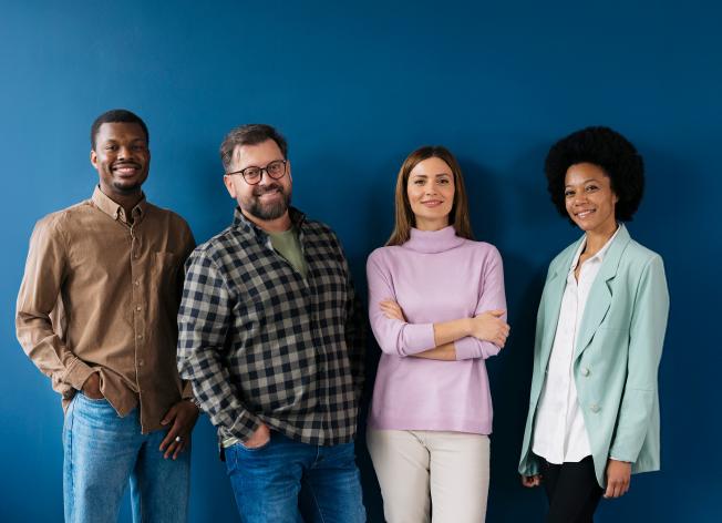 Ihmisiä seisoo sinisen seinän edessä ja hymyilee