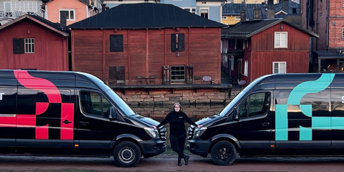 Kaksi mustaa pakettiautoa nokat vastakkain. Autojen välissä seisoo Mervi Svensk. Autoissa lukee Sukittajat