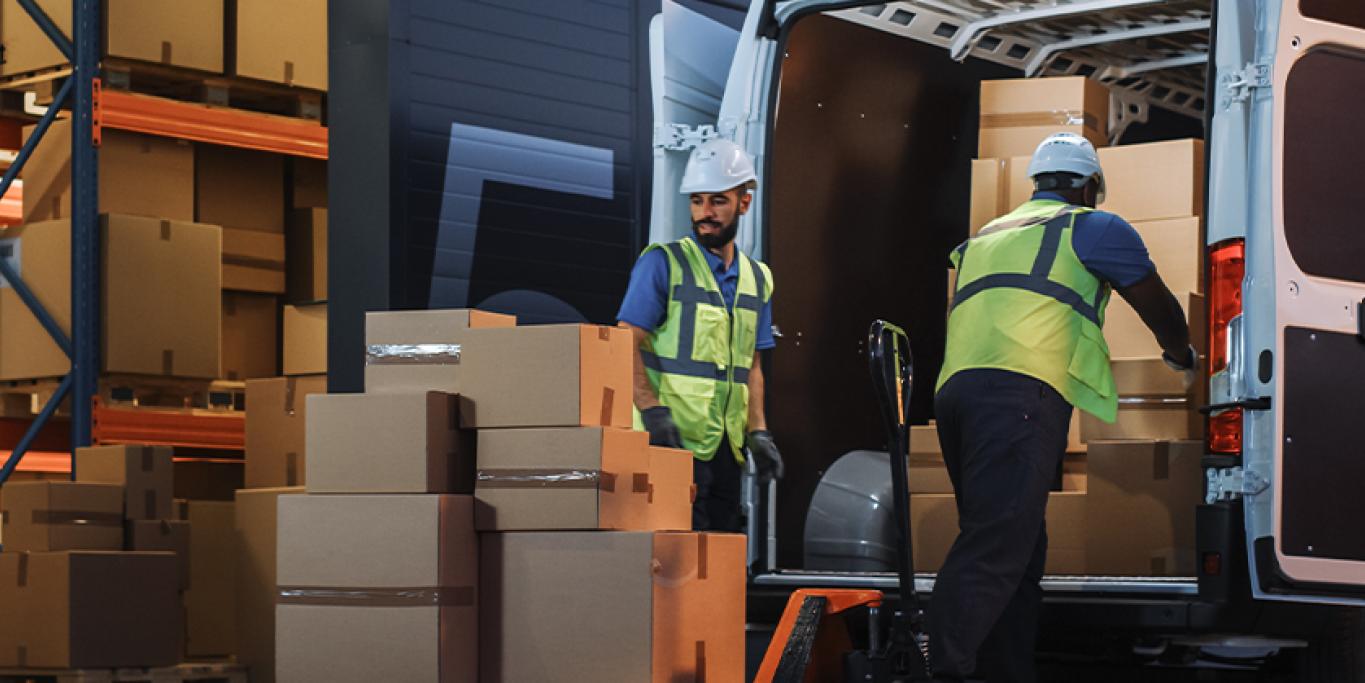 Kaksi henkilöä varastossa lastaa pakettiautoa