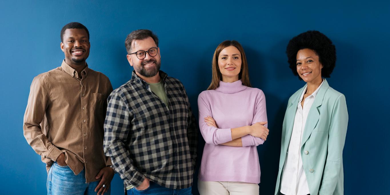 Ihmisiä seisoo sinisen seinän edessä ja hymyilee