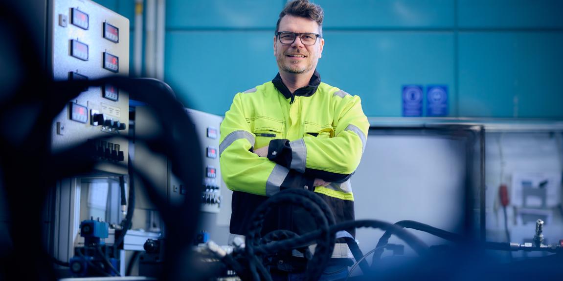 Mies työtakkipäällä hydrauliikkapenkin vieressä.