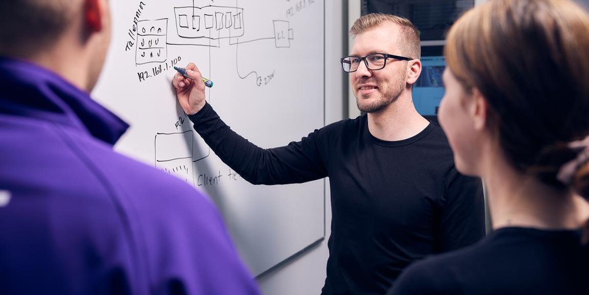 Kolme ihmistä valkotaulun edessä opetustilanteessa
