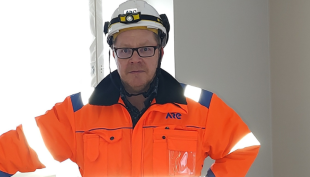 Jouni Riikola seisoo talotekniikkakohteessa työvaatteissa. Hän katsoo kameraan, ja hänellä on päässään suojakypärä. Kuva on artikkelin kansikuva, joten se rajautuu siten, että Jounista näkyy ainoastaan ylävartalo.