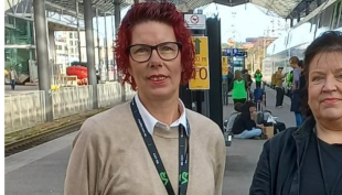 Ann-Mari Ahonen ja Helena Tikka seisovat rautatieasemalla. heidän takanaan on juna ja junaraide. 